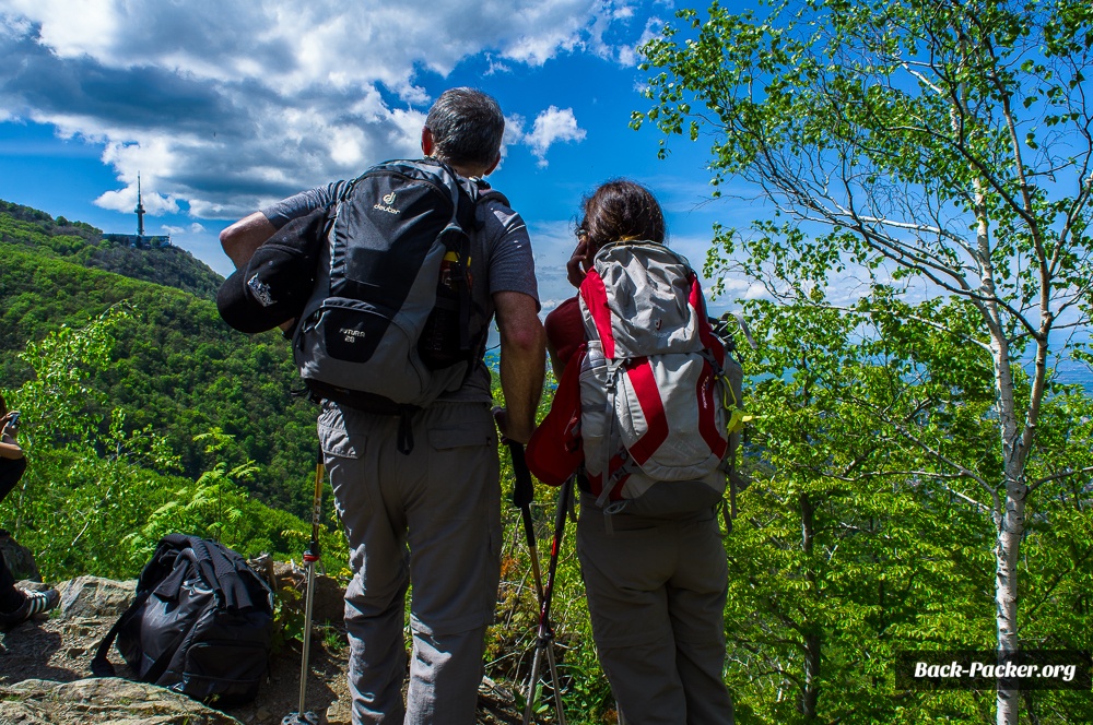 Blick auf 2 Wanderer die auf einem Aussichtspunkt bei einer Vitosha Wanderung stehen und über den Berg und Wald blicken