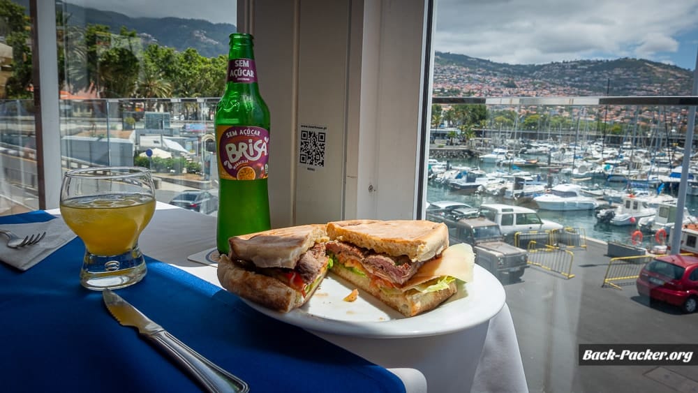 Blick auf ein Prego Sandwich mit Limonade, im Hintergrund sind Boote und der Yachthafen von Funchal zu erkennen